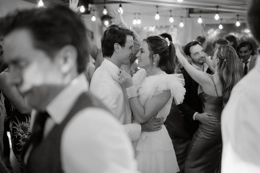 A romantic black and white shot of couples dancing at a wedding reception under string lights.
