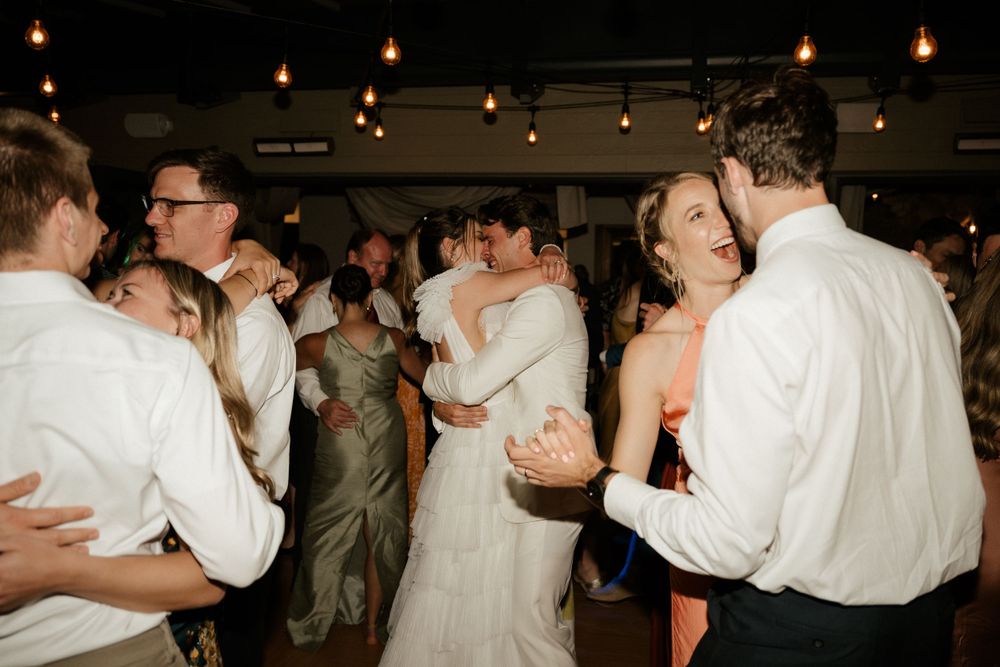 Wedding guests dancing in a dimly lit reception venue with hanging lights.