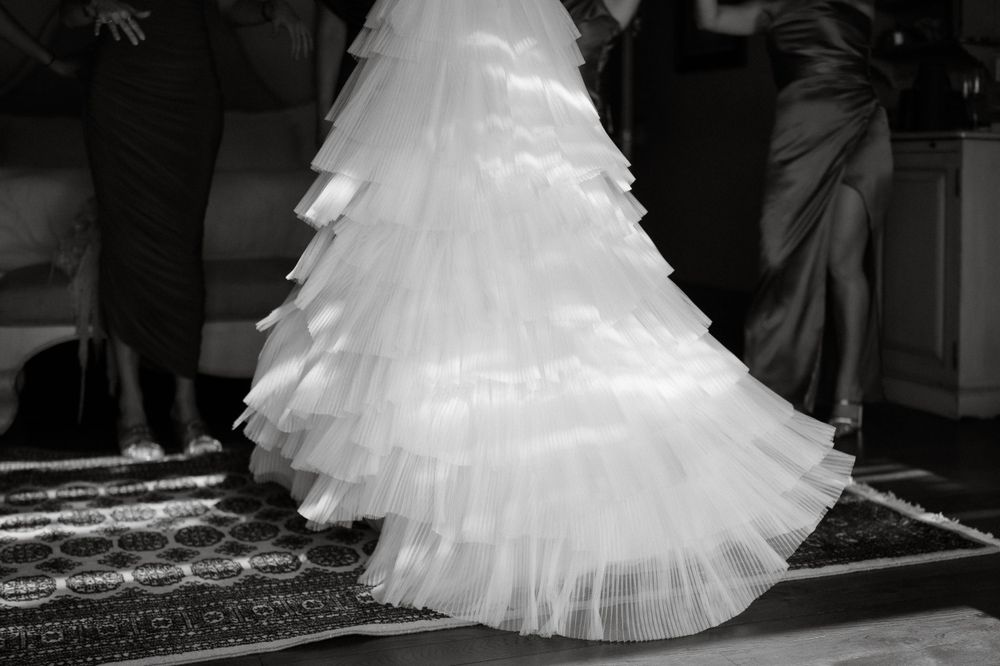Black and white photograph of a layered tulle wedding dress train on a patterned carpet.