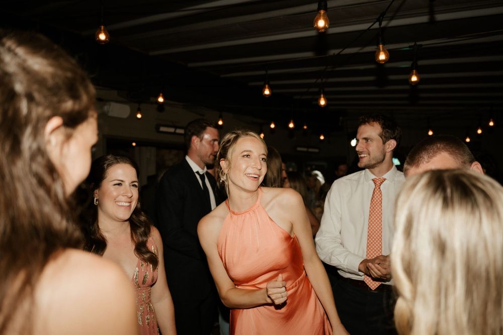Wedding guests socializing and dancing at reception under warm ceiling lights.