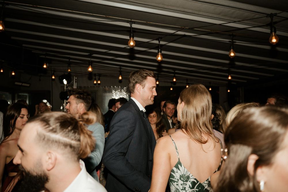 Crowded dance floor under string lights at an elegant indoor reception venue.