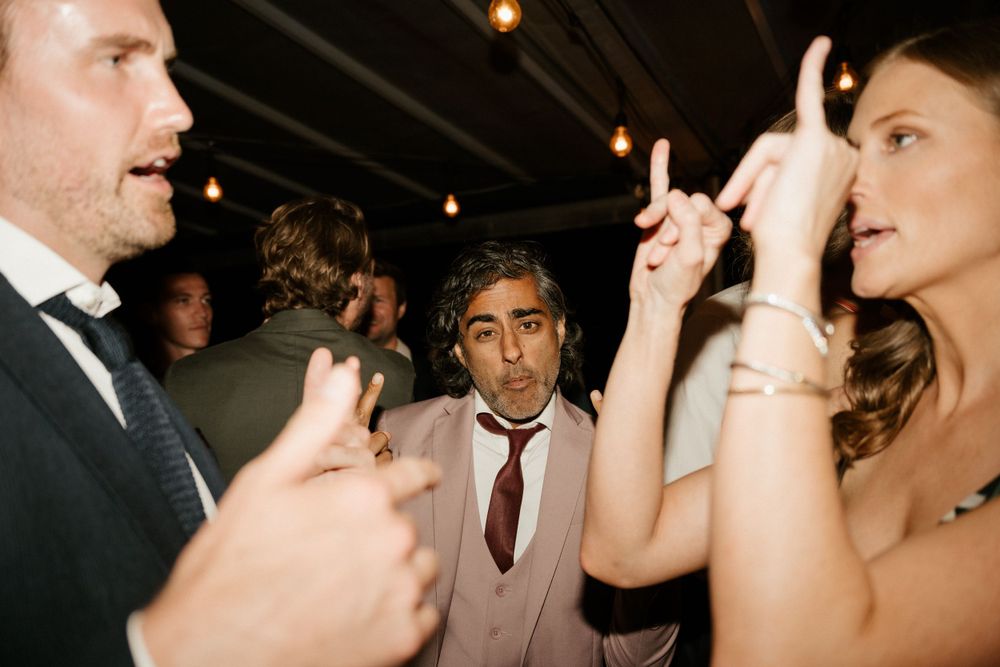 Party guests in formal attire socializing and dancing under dim lighting.