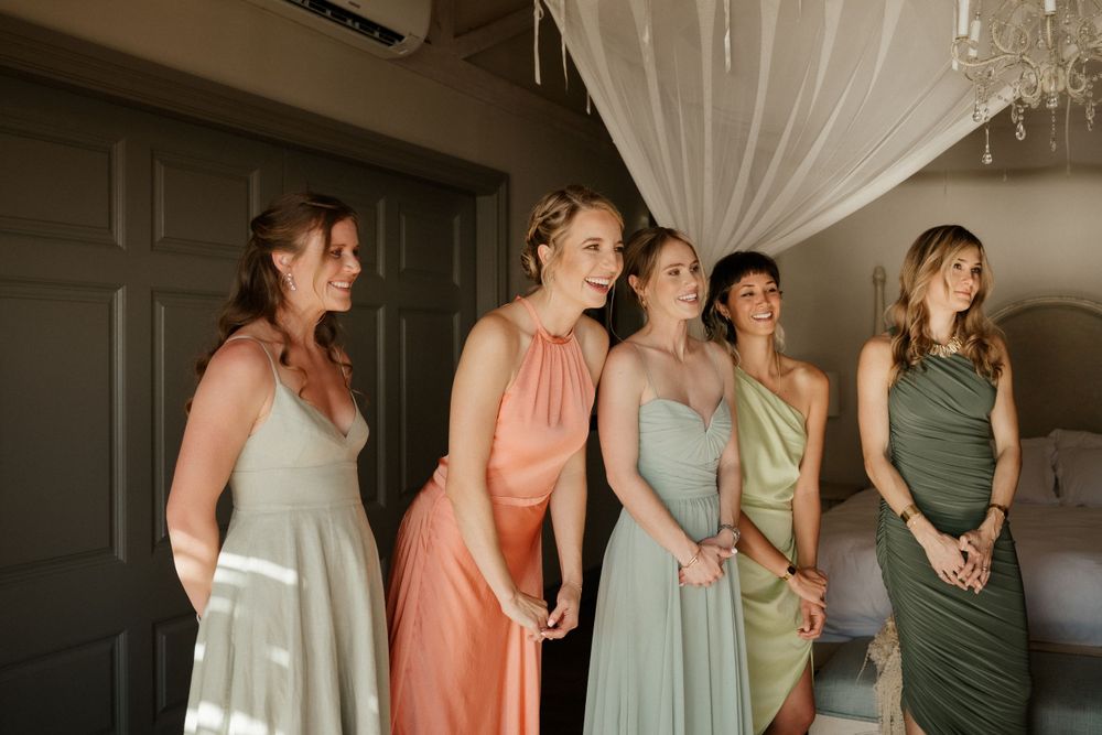 A row of bridesmaids in pastel-colored dresses stand together in an elegant indoor setting.