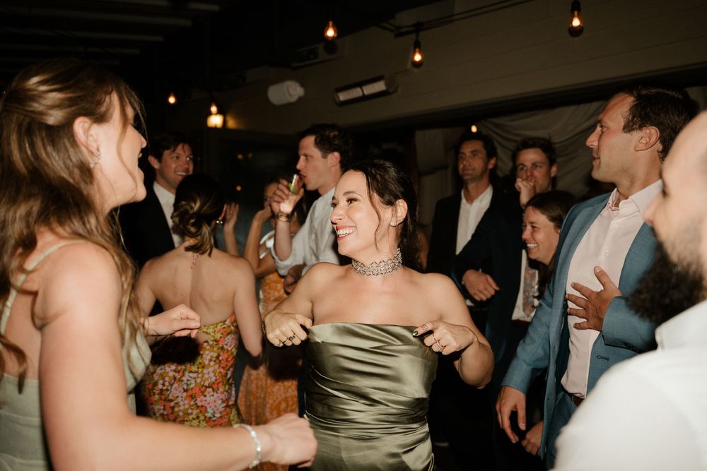 Energetic dance party scene at a wedding reception with guests dancing under string lights.