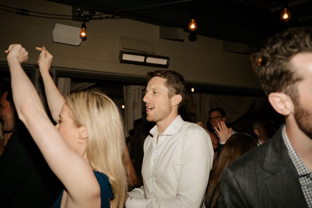 Party guests dancing and celebrating with raised arms at an indoor event.