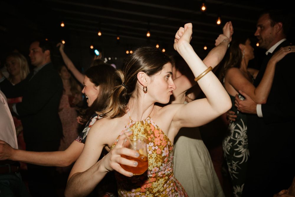 A wedding guest in a floral dress dances with raised arms at the reception party.