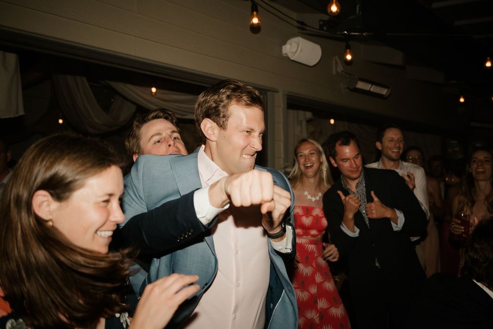 Wedding guests dancing energetically at a lively reception celebration with overhead string lights.
