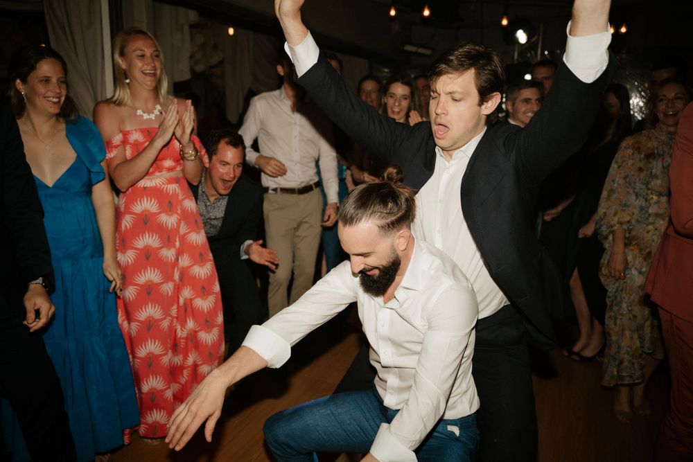 Guests dancing energetically at a wedding reception with colorful dresses in background.