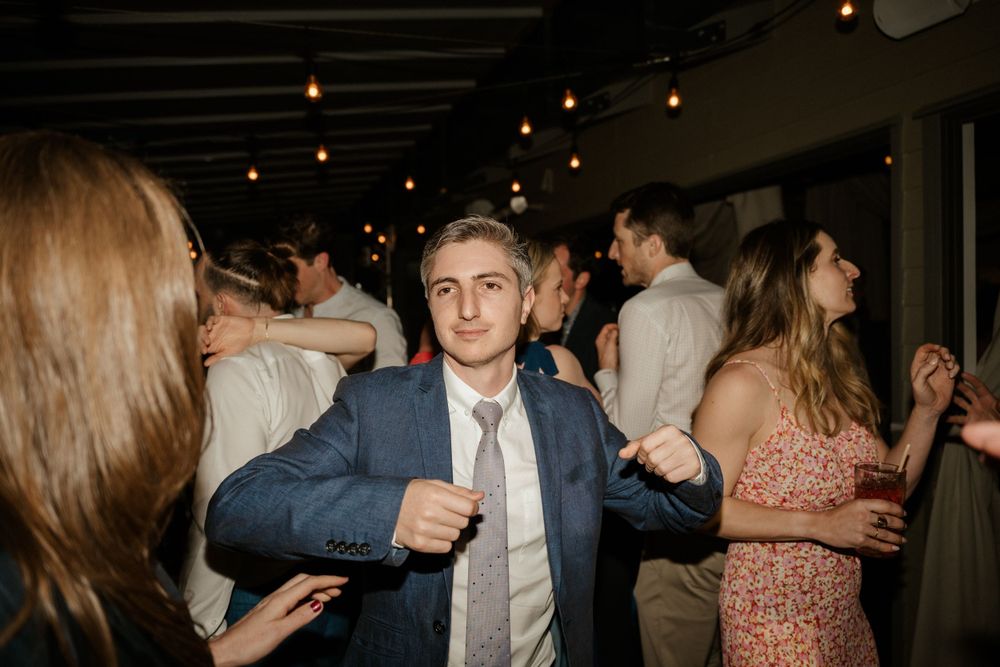 Wedding guests dancing and celebrating at a dimly lit indoor reception venue.