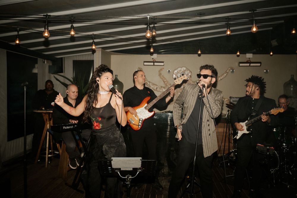 Live band performing on stage with singer and instruments at indoor venue.