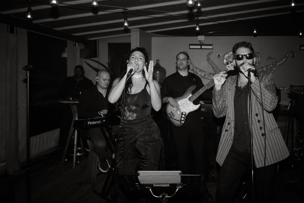 Black and white photo of band members performing energetically on stage with instruments.