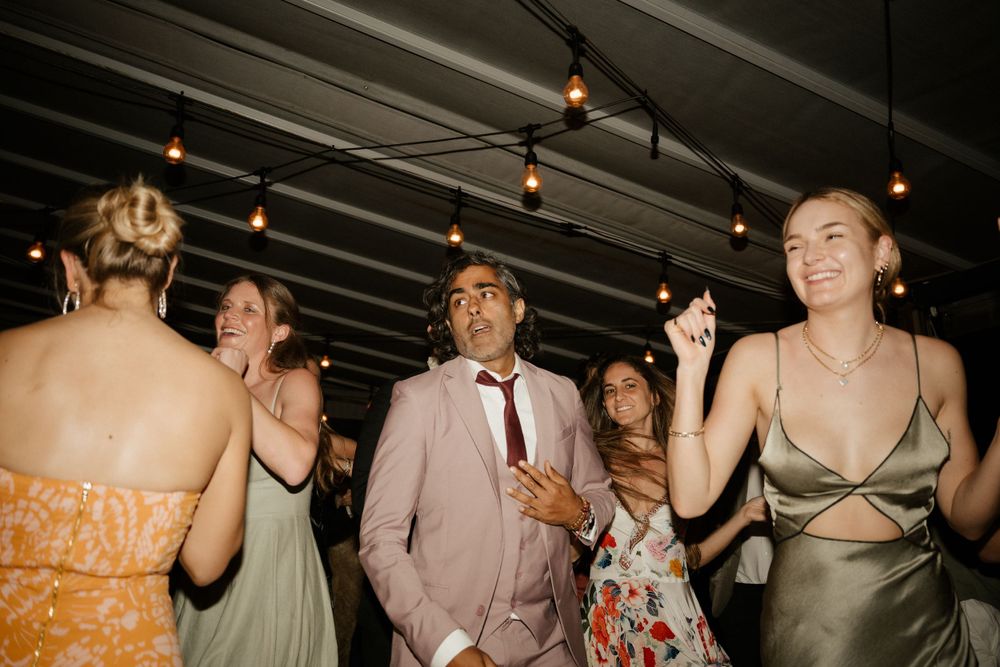 Wedding guests dancing under string lights at evening reception.