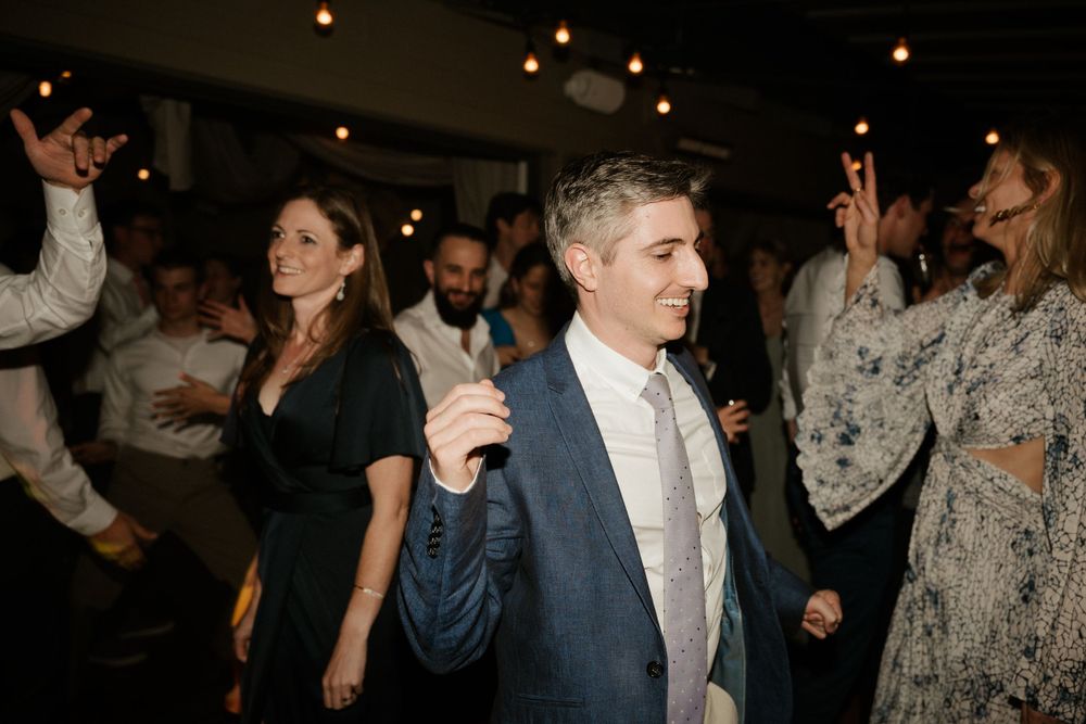 Wedding guests enjoying themselves on a dark dance floor illuminated by overhead string lights.