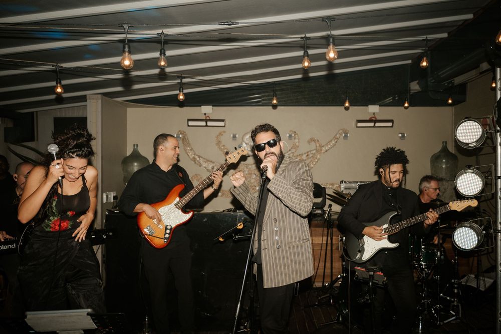 Live band performs with guitars and drums at indoor wedding reception.