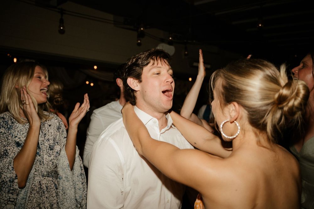 Wedding guests dance energetically at reception party under string lights.