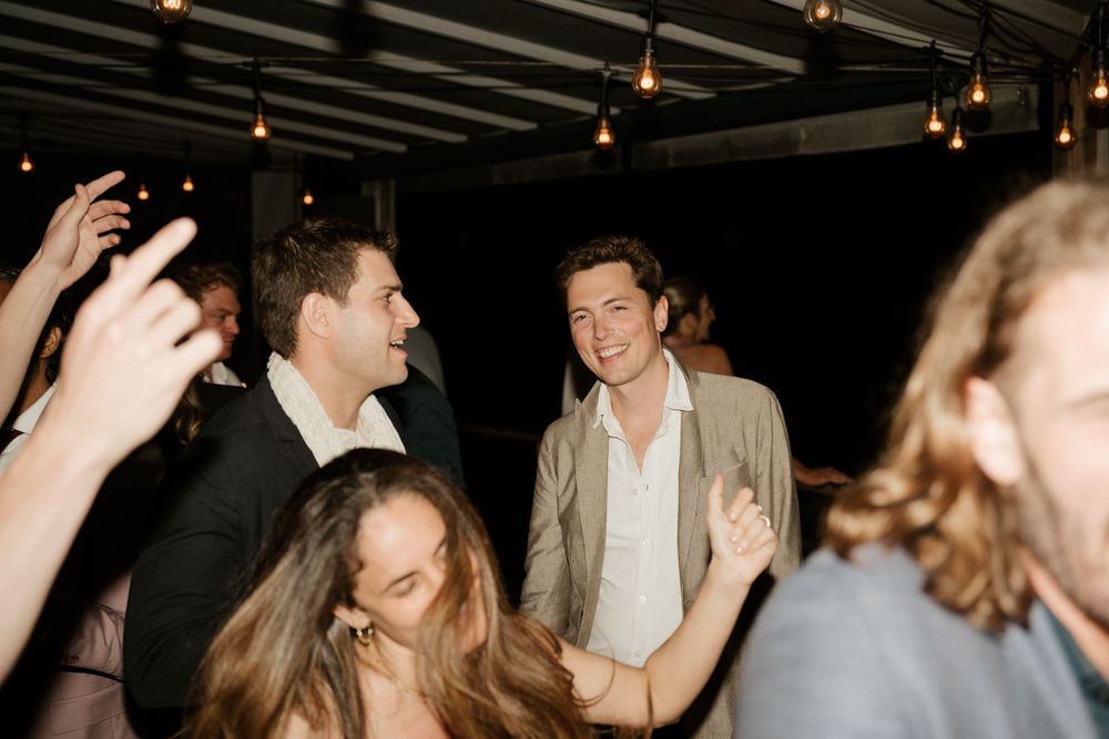 Wedding guests dancing and celebrating under dark wooden beams with string lights.