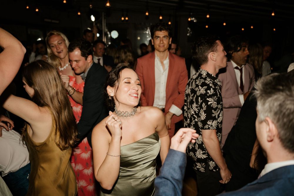 Wedding guests dancing and celebrating at an evening reception under moody lighting.