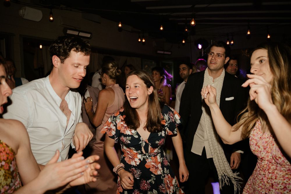 Wedding guests dancing and laughing together at a lively indoor reception party.
