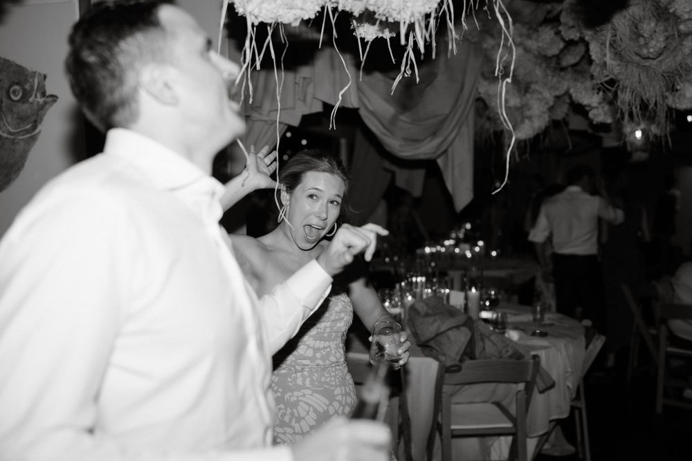 Black and white candid photo of guests celebrating at a lively wedding reception.