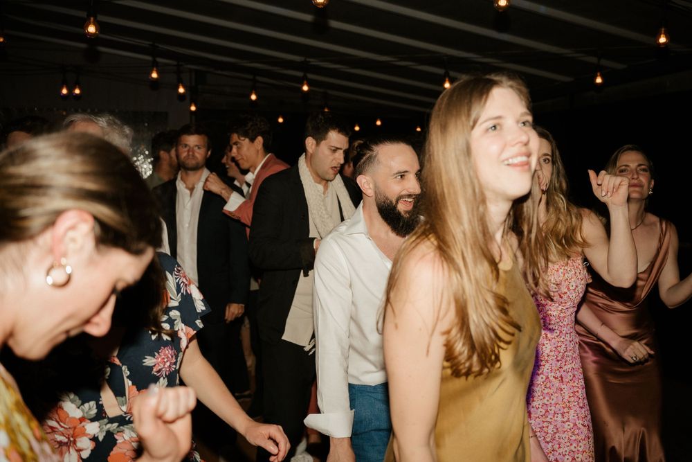 Lively dance floor scene at a wedding reception with guests dancing under string lights.