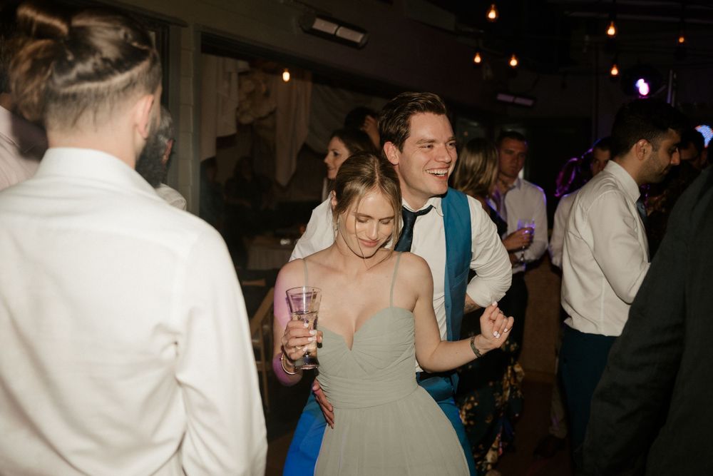Wedding reception guests dancing and celebrating on dimly lit dance floor.