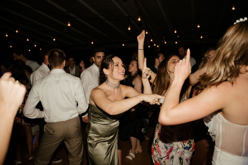 Wedding guests dancing and celebrating with raised arms on a dimly lit dance floor.