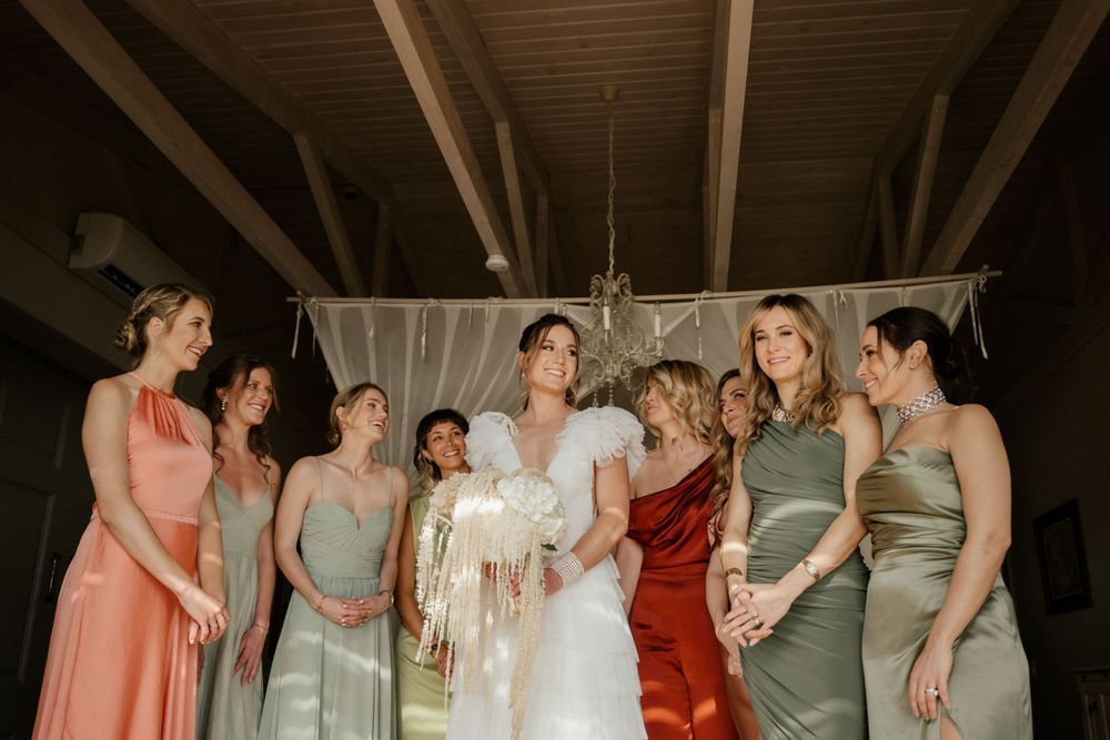 Wedding party in pastel and jewel-toned dresses gathered in a rustic venue.