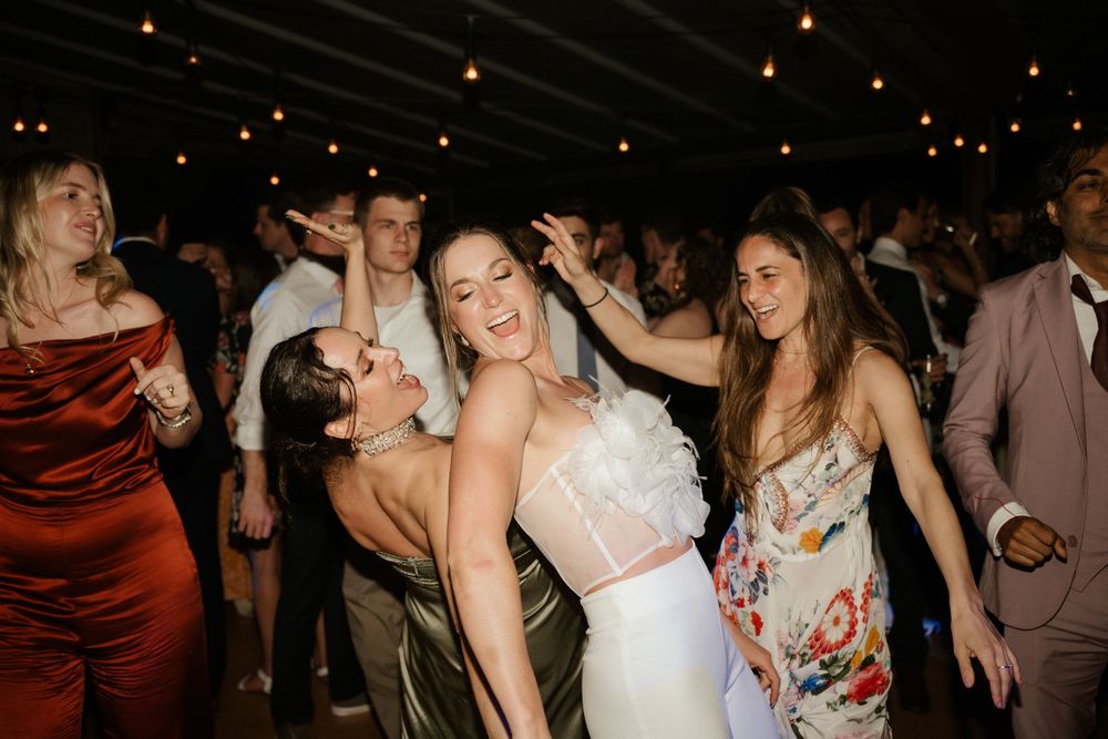 Wedding party dances enthusiastically under dimly lit reception venue.