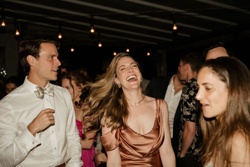 Guests dancing and laughing together at a lively wedding reception under string lights.