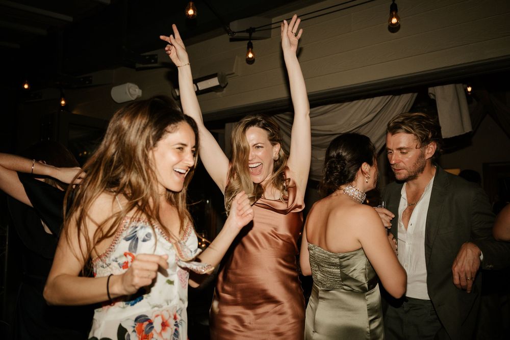 Guests dancing and celebrating at a wedding reception with string lights overhead.
