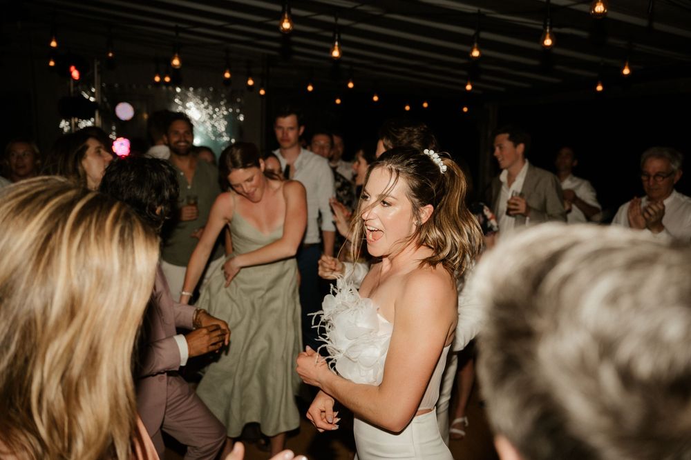 Wedding reception celebration with guests dancing under warm string lights.