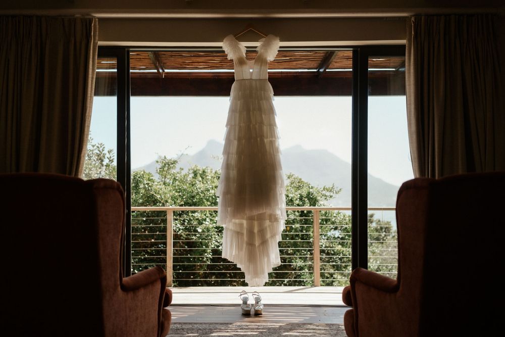 Wedding dress hanging in doorway silhouetted against mountain landscape view.