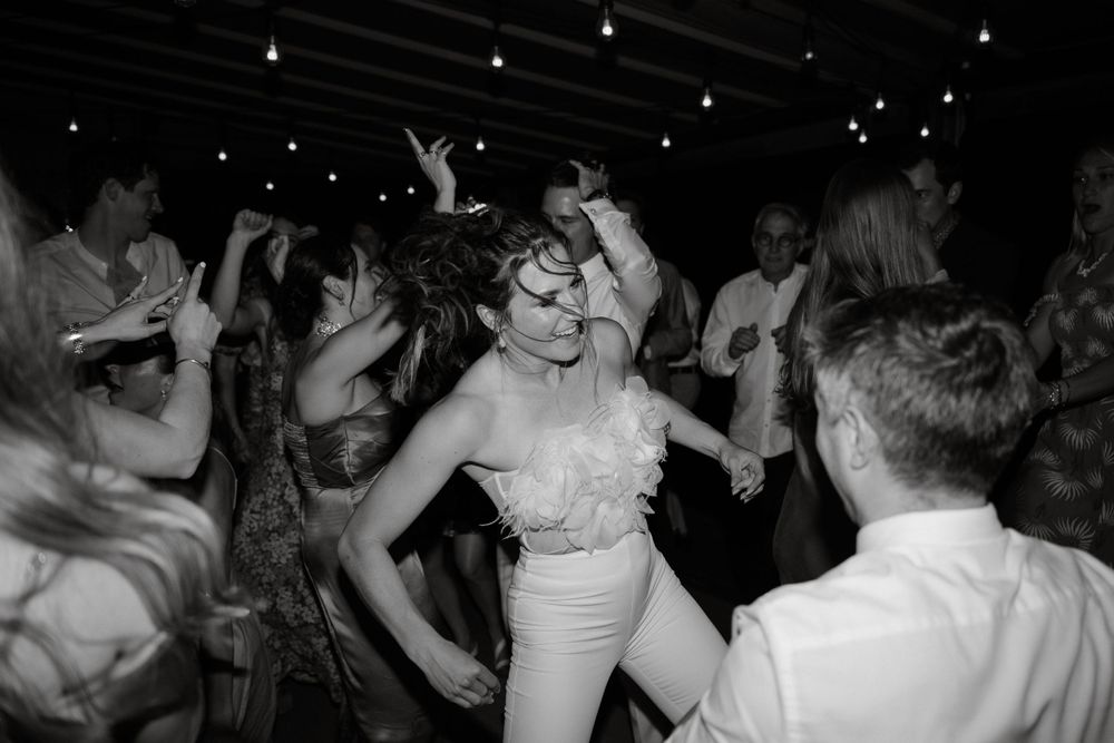 Wedding guests dance enthusiastically on a dark dance floor under dramatic lighting.