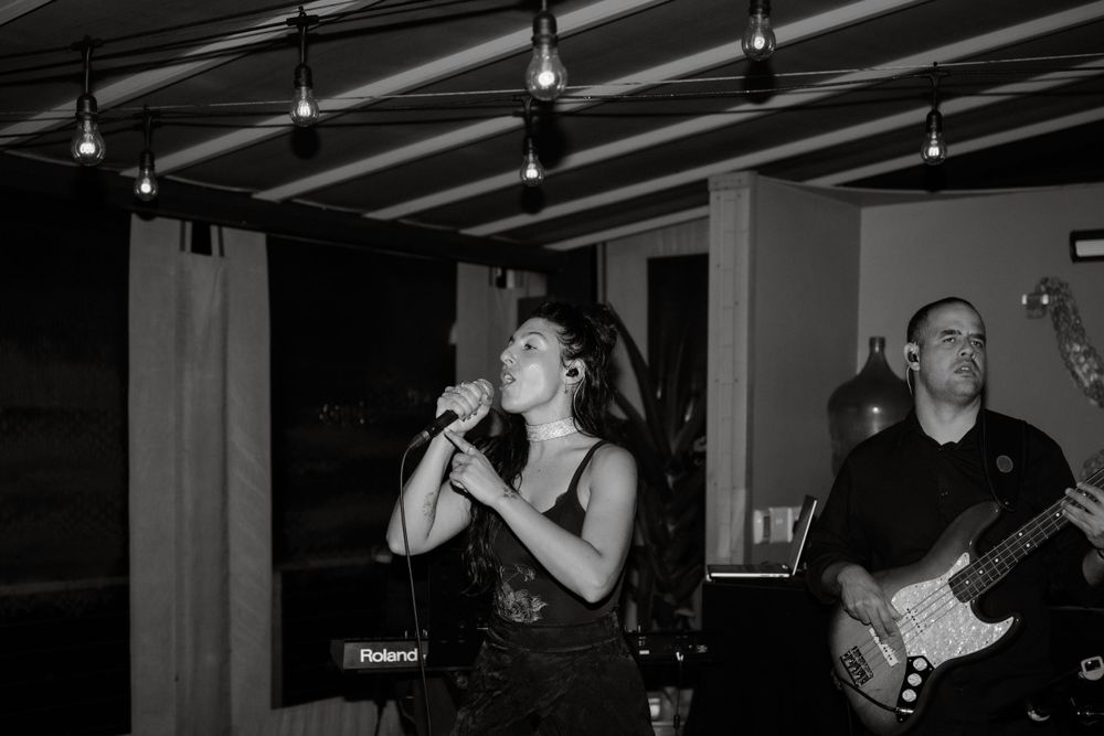 Black and white photo of band performing at indoor venue with string lights.