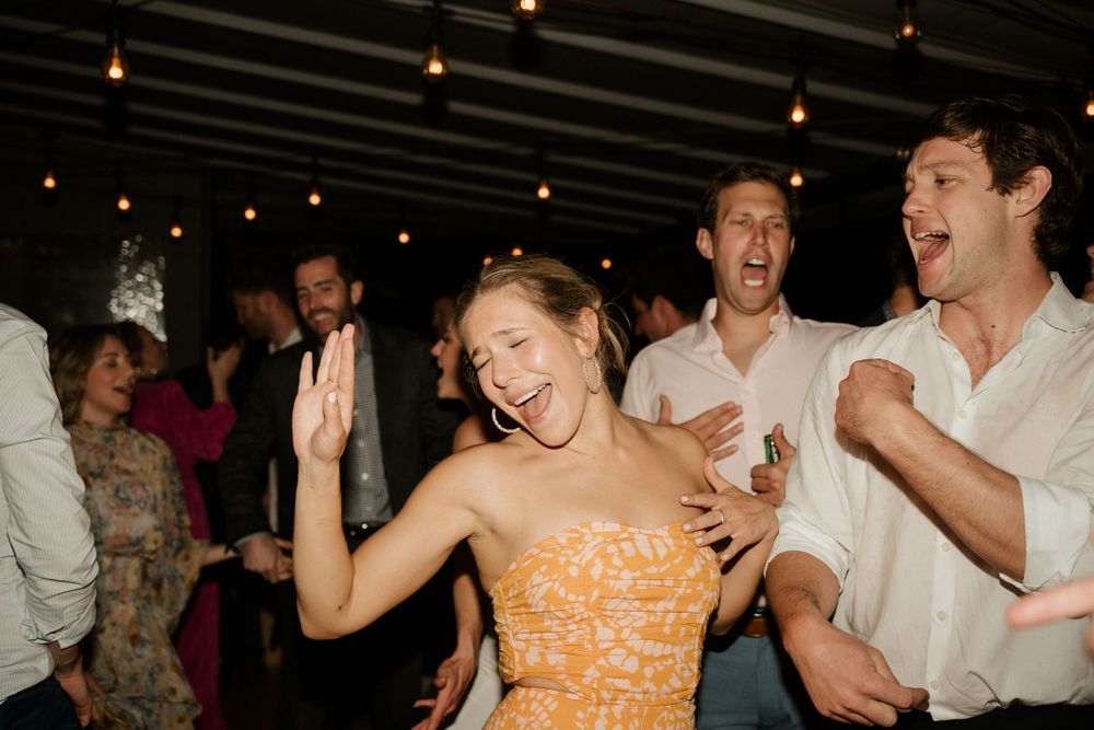 Party guests dance enthusiastically under pendant lights at a lively indoor celebration.