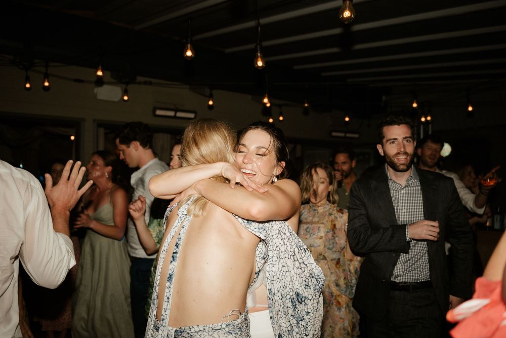 Wedding guests sharing hugs and embraces during a reception under string lights.