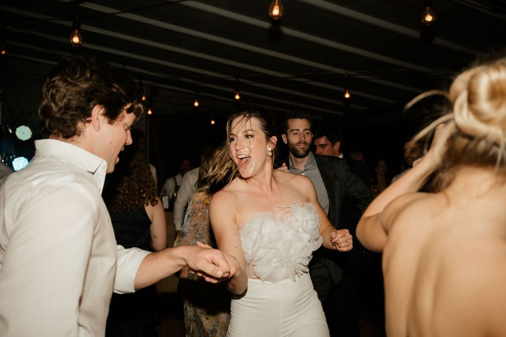 Wedding guests dancing joyfully under string lights at indoor reception.