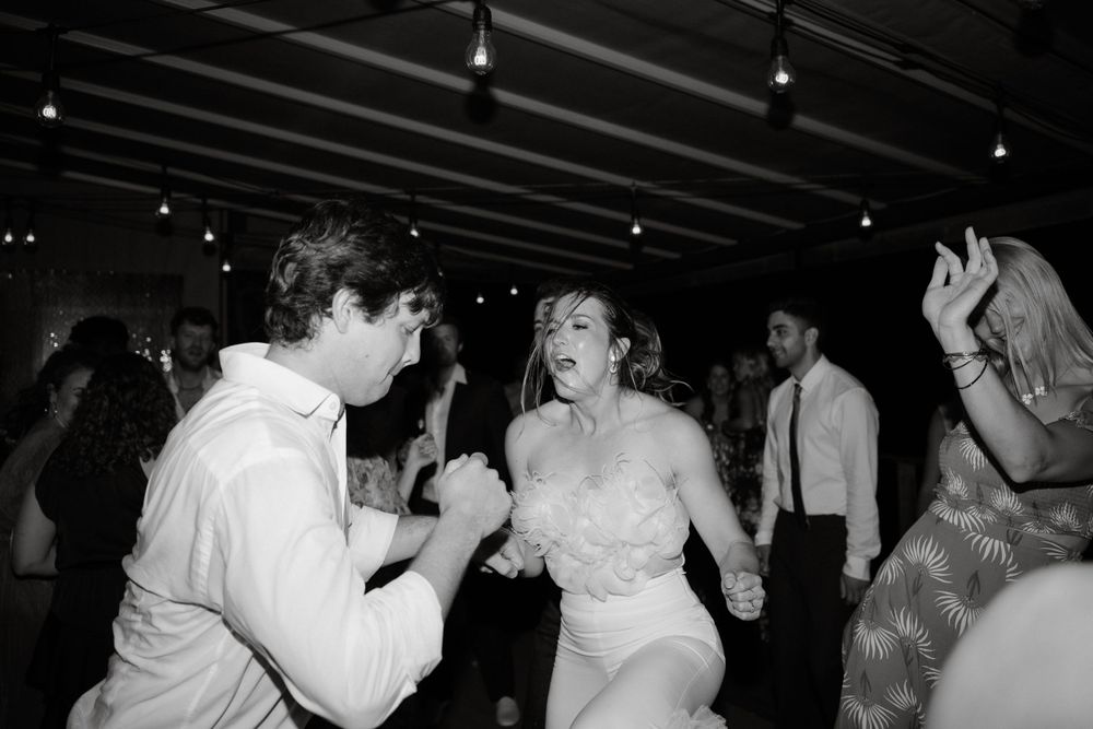Black and white photo of wedding guests dancing energetically at a reception.