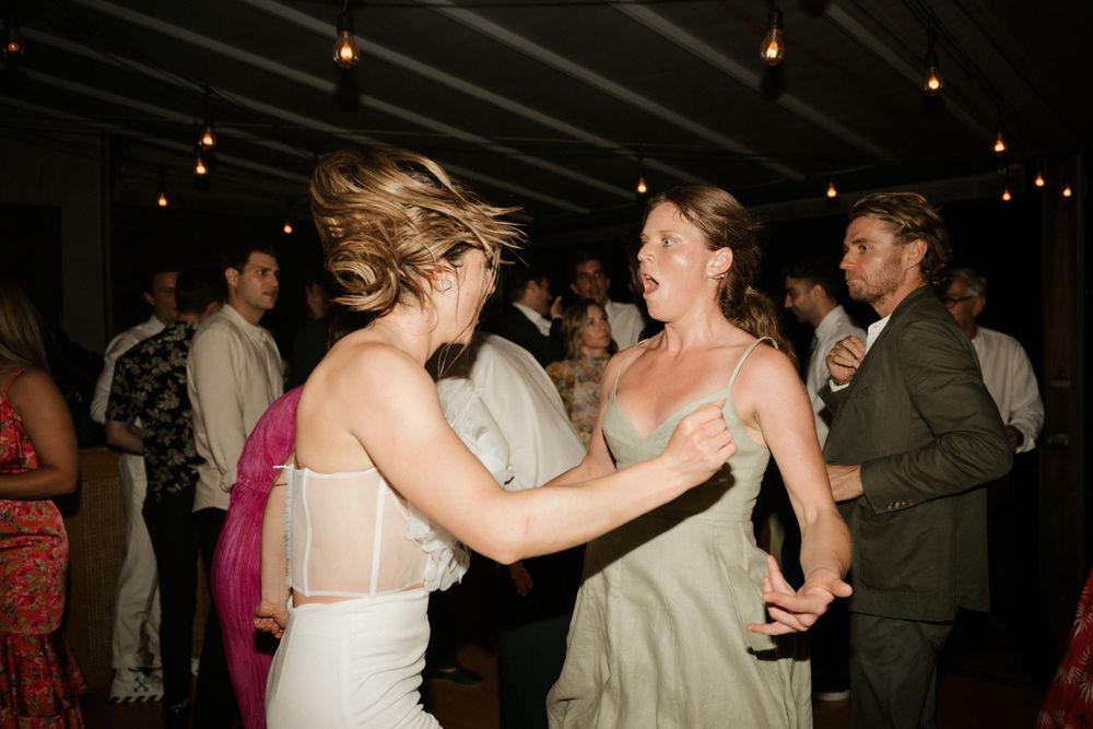 Wedding guests dancing energetically at a dimly lit indoor reception venue.