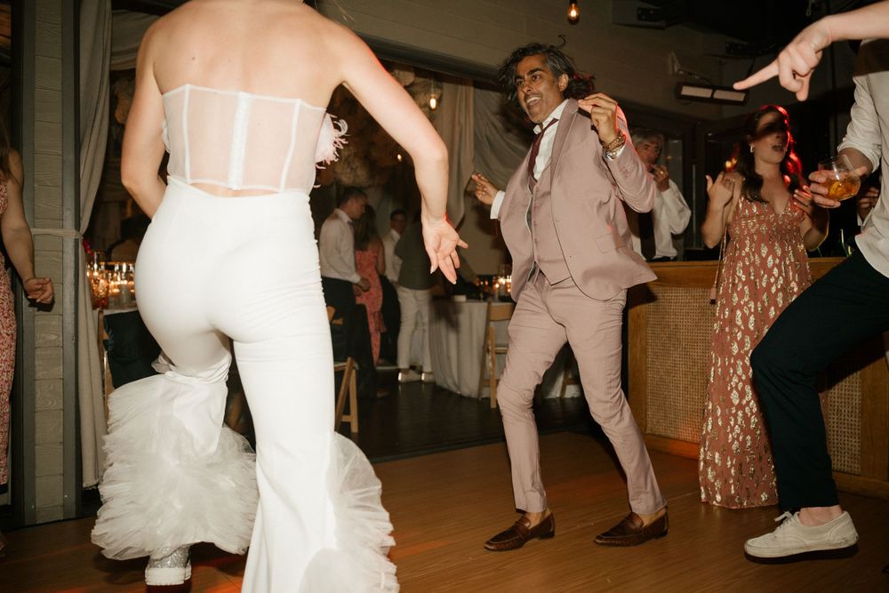Wedding guests dancing together in formal attire under ambient lighting.