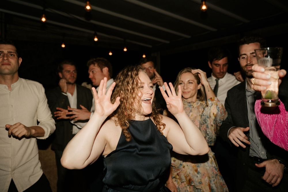 A guest dances enthusiastically at a wedding reception under string lights.