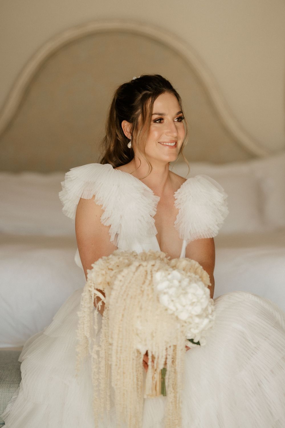 A bride in a white feathered wedding dress holds a cascading bouquet.