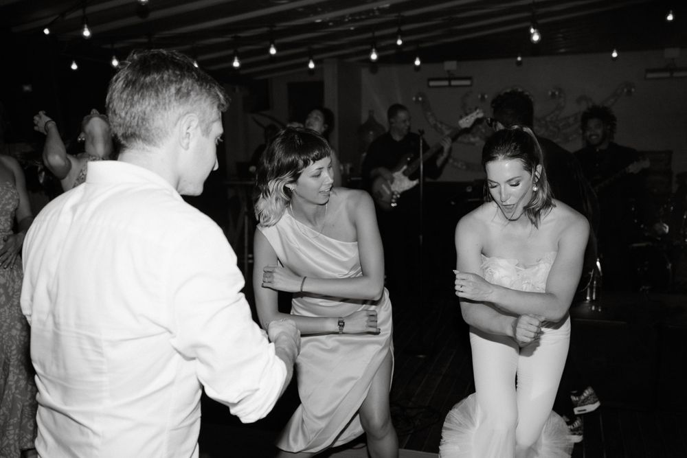 Wedding guests dancing and laughing together in black and white at an indoor celebration.