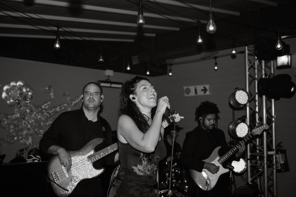 A live band performs on stage with instruments and lighting equipment in black and white.