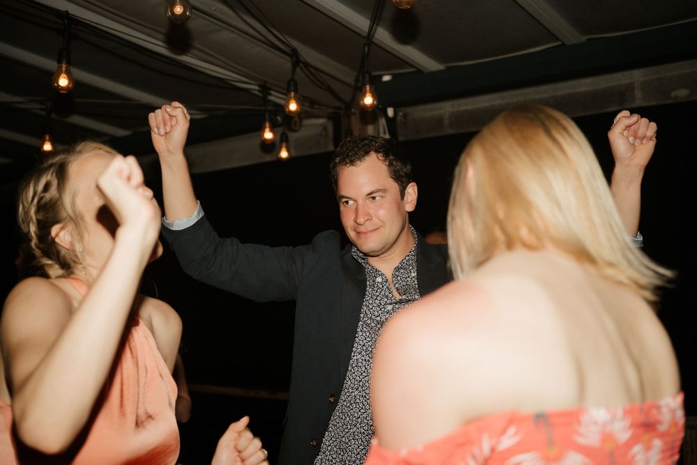 Wedding guests dancing enthusiastically under dim lighting at an indoor reception.