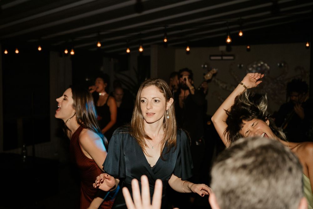 People dancing at a dimly lit party with hanging lights overhead.
