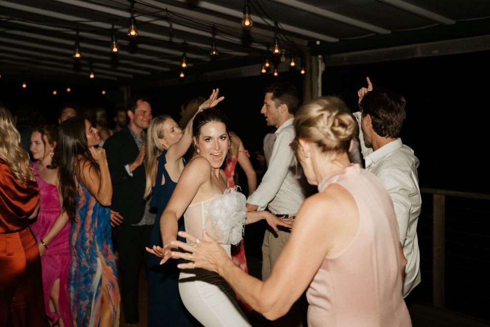 Wedding guests dancing and celebrating on a dimly lit dance floor at the reception.