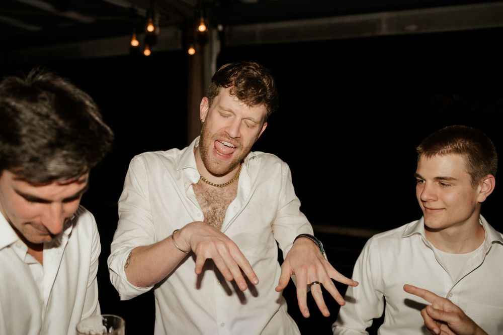 Three guests in white shirts sharing a jovial moment during the wedding reception.