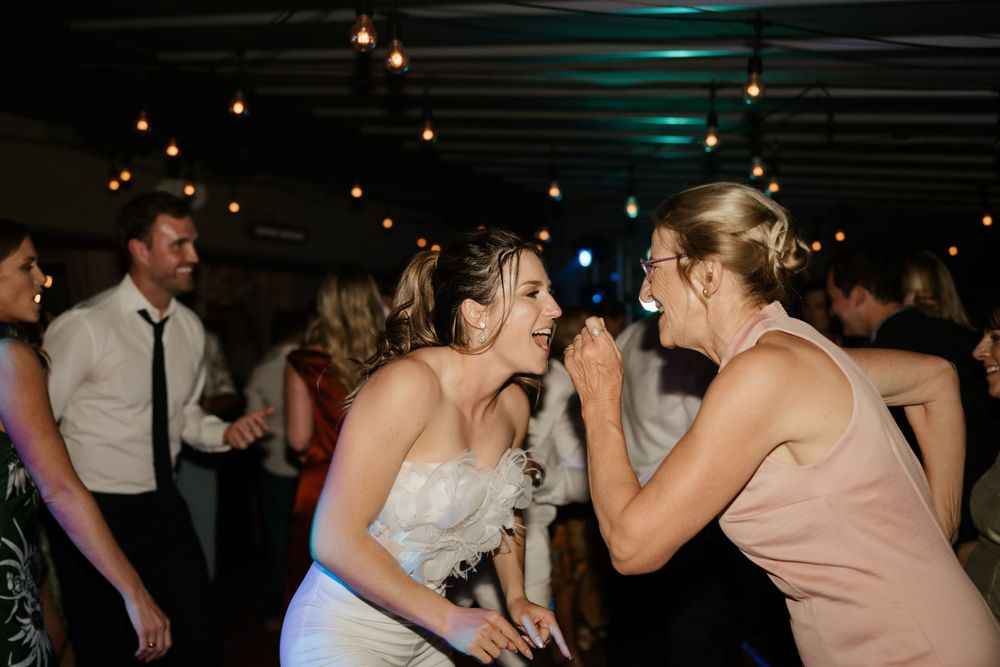Two wedding guests share a joyful laughing moment on the dance floor.