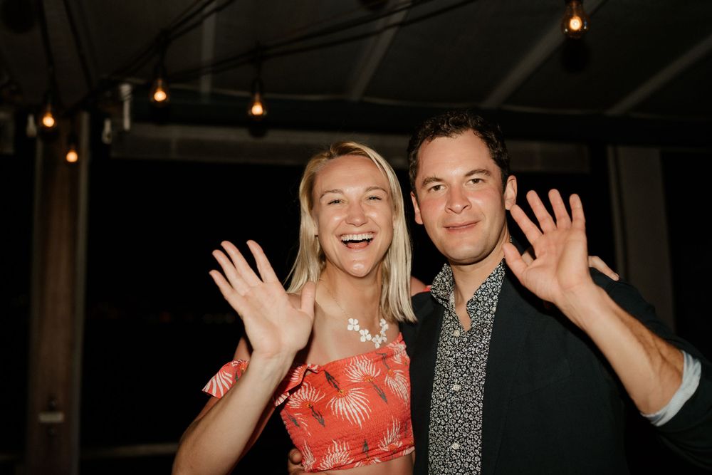 Energetic party guests wave and laugh during festive evening celebration.